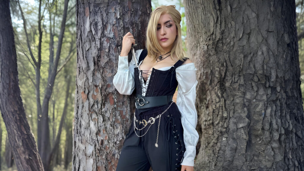 Woman in pirate-inspired outfit featuring lace-up pirate pants, a corset top, and celestial belt, standing against a tree in a forest setting.