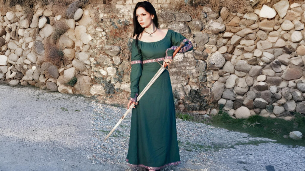 Woman in flowing medieval dress posing in a forest with sunlight filtering through trees