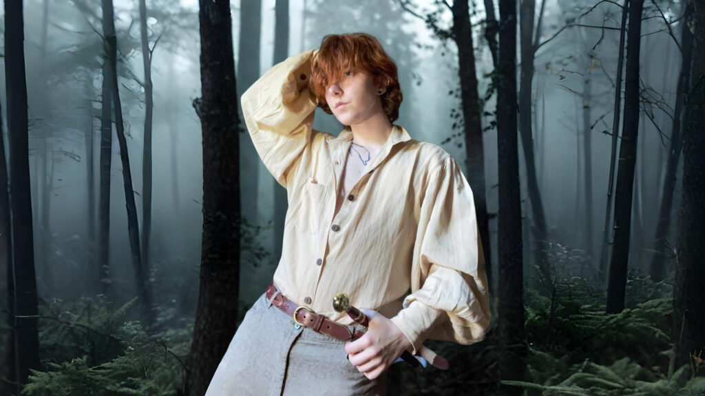 Model wearing a classic cream pirate shirt from The Pirate Dressing, styled with a leather belt and sword, posing in a misty forest backdrop.